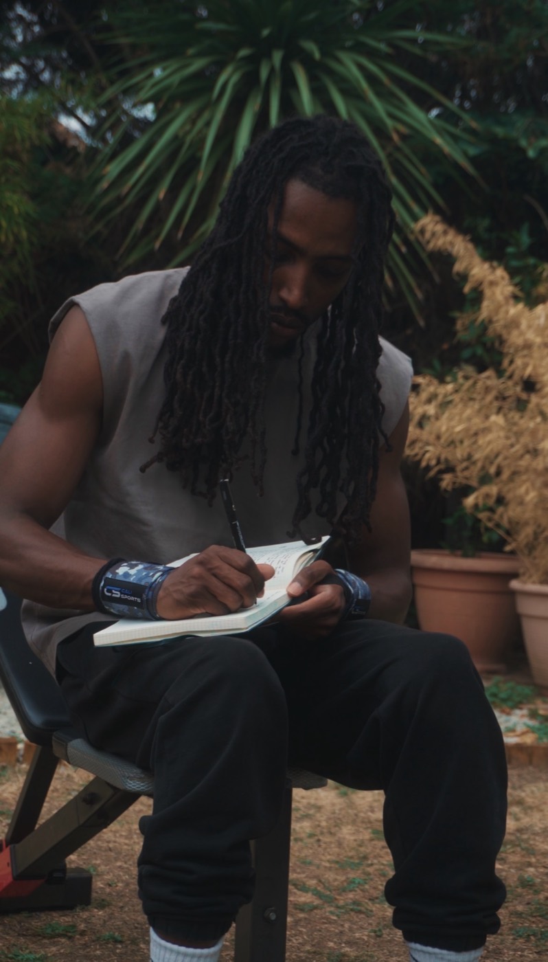 Reece sitting in a garden, writing in a notebook